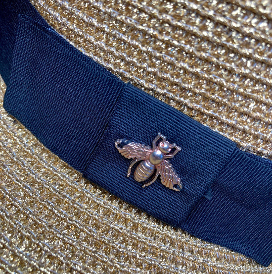 A close up of the hat's gold & shiny Bee, stiched onto the ribbon